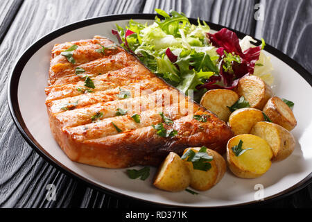 Fried swordfish steak with baby potatoes and fresh salad close-up on a plate on a wooden table. horizontal Stock Photo