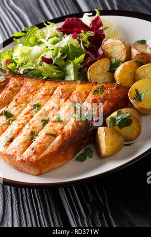 Grilled swordfish fillet with fried potatoes and fresh salad close-up on a plate on a wooden table. vertical Stock Photo