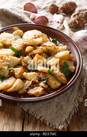 Jerusalem artichokes roasted with garlic, cheese and parsley closeup on a plate on the table. vertical Stock Photo