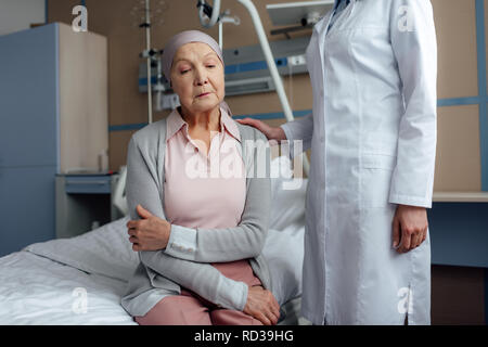 female doctor consoling upset senior woman with cancer and arms crossed in hospital Stock Photo