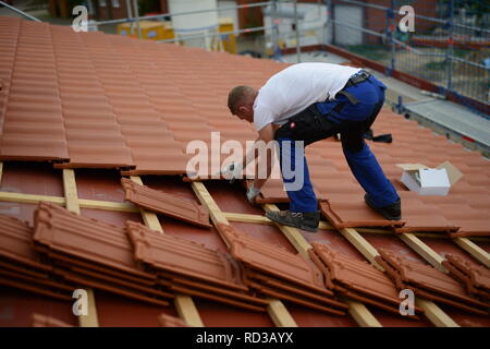 Dach Baustelle neu mit roten Dachziegeln. Dachdecker Bauarbeiter in weißem T-Shirt und Arbeitshandschuhen in Deutschland. Mann bei der Arbeit. Stock Photo