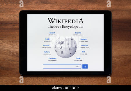 The website of Wikipedia is seen on an iPad tablet, which is resting on a wooden table (Editorial use only). Stock Photo