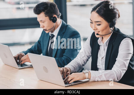 young kazakh coworkers in headsets using laptops at workplace Stock Photo