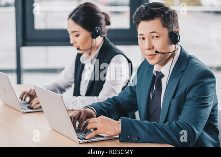 young man in headset looking at camera while working with female colleague in call center Stock Photo