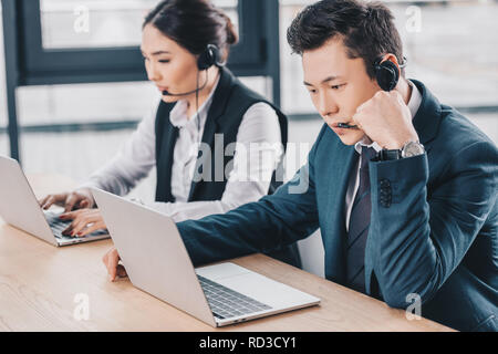young call center operators in headsets using laptops in office Stock Photo