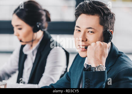 handsome young man in headset smiling at camera while working with female colleague in call center Stock Photo