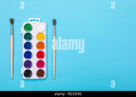Watercolor paints and brushes in white box, isolated on blue background Stock Photo