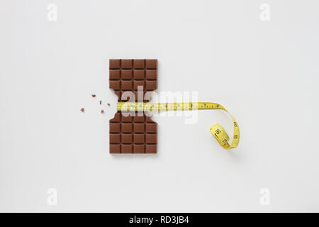 Block of chocolate bar with sides bitten off and chocolate crumbs with a tape measure around the middle Stock Photo