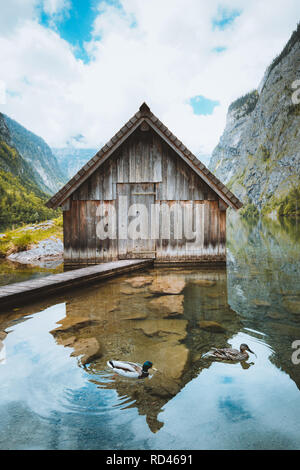 Idyllic view of traditional old wooden boat house at scenic Lake Obersee on a beautiful sunny day with blue sky and clouds in summer, Bavaria, Germany Stock Photo