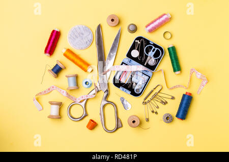 Composition with threads and sewing accessories - scissors, centimeter, pins on yellow background. Stock Photo