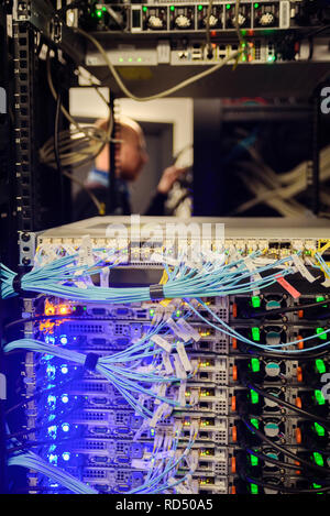 Young man engineer working with network hardware. Focus on rack Stock Photo