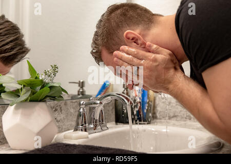 Good Looking Young Man Washing Hands and Face in Home Bathroom Mirror and Sink Getting Clean and Groomed During Morning Routine Stock Photo