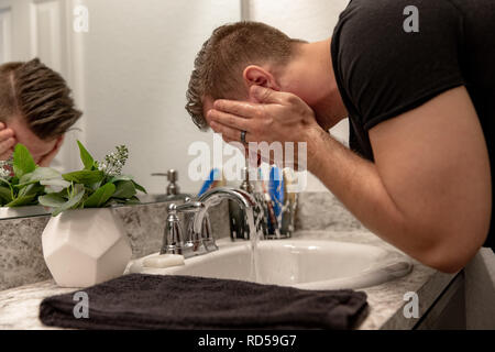 Good Looking Young Man Washing Hands and Face in Home Bathroom Mirror and Sink Getting Clean and Groomed During Morning Routine Stock Photo