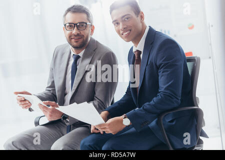 two professional businessmen smiling at camera while working with papers and digital tablet in office Stock Photo