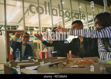 Multi-ethnic group of students eating pizza at university canteen. Students hanging out at university campus cafe. Stock Photo