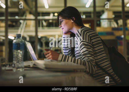Female student taking notes from a laptop at library. Young caucasian woman sitting at table doing assignments in college library. Stock Photo