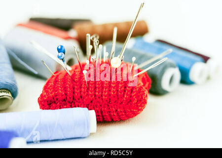 Red knitted needle pad for sewing and colored thread coils on white background Stock Photo