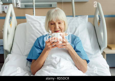 senior woman lying in bed and drinking tea in hospital Stock Photo