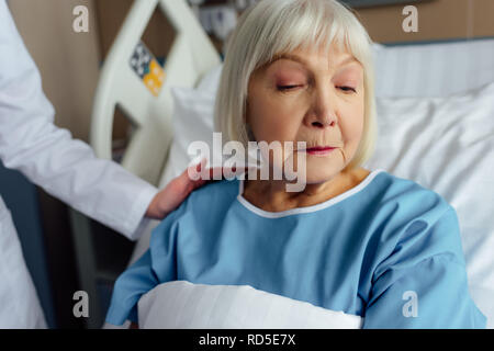 female doctor consoling upset senior woman with grey hair lying in hospital bed Stock Photo