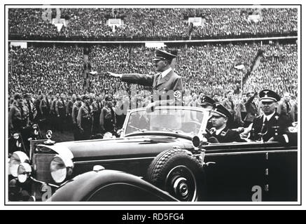 Adolf Hitler in uniform wearing swastika armband gives Heil Hitler salute to the military and crowds at a huge Nazi rally in 1938 Germany. Hitler salutes attendees at a Reichsparteitag (Reich Party Day) in Nuremberg, Germany. A uniformed Martin Bormann also in attendance sitting in rear of open top Mercedes Car Stock Photo