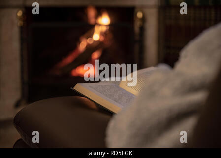 Woman resting with book near fireplace Stock Photo