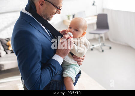 businessman in suit feeding infant daughter from bottle Stock Photo