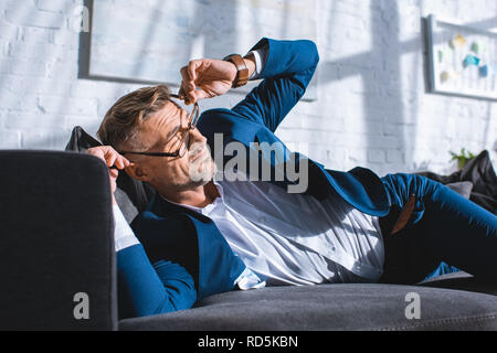 drunk businessman wearing glasses while lying on sofa Stock Photo