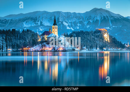 Beautiful twilight view of Lake Bled with famous Bled Island and historic Bled Castle in the background during scenic blue hour at dawn in winter, Slo Stock Photo