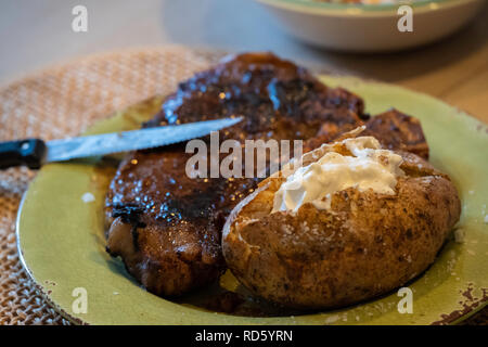 A seared ribeye, or rib eye steak cooked to medium well done with a baked potato and sour cream on a dinner plate. USA. Stock Photo