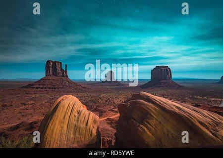Classic panoramic view of scenic Monument Valley with the famous Mittens and Merrick Butte illuminated in beautiful mystic moonlight on a starry night Stock Photo