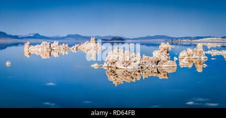 Panoramic view of fascinating tufa rock formations mirrored on calm water surface of famous Mono Lake on a beautiful sunny day with blue sky in summer Stock Photo