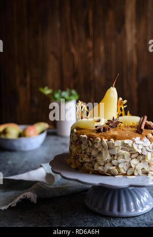 Delicious layered cake with caramel glaze, decorated with almond slices, pears, spun sugar decorations and cinnamon sticks Stock Photo