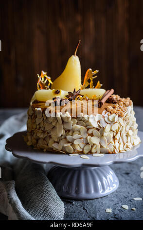 Delicious layered cake with caramel glaze, decorated with almond slices, pears, spun sugar decorations and cinnamon sticks Stock Photo