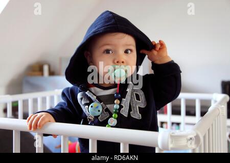 Little boy, 10 months, in the cot with pacifier and hoodie Stock Photo
