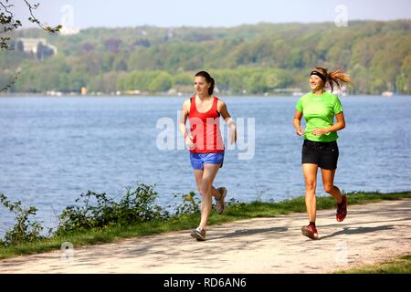 Two recreational runners, young women, 25-30 years, jogging on a lakeside path Stock Photo