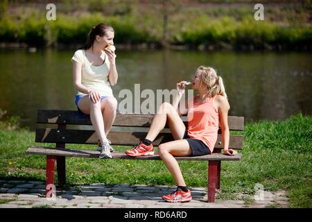 Young women, 25-30 years, eating on a bench after exercise Stock Photo
