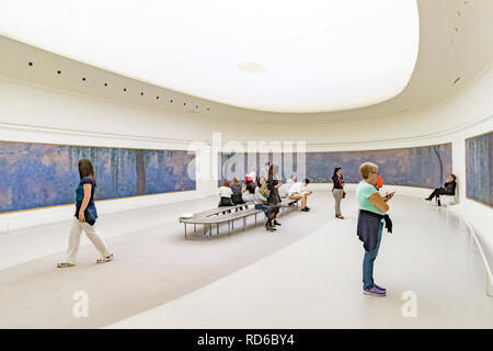 People looking at the Water Lilies by Claude Monet set in curved panels in an oval shaped room at The Orangerie or Musee de l'Orangerie ,Paris, France Stock Photo