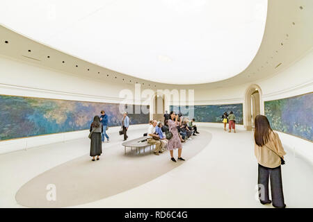 People looking at the Water Lilies by Claude Monet set in curved panels in an oval shaped room at The Orangerie or Musee de l'Orangerie ,Paris, France Stock Photo