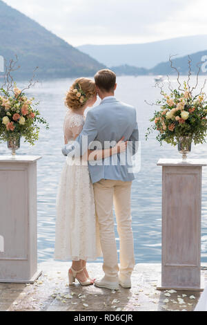 newlywed couple stands embracing against the sea between the stands with flower arrangements after the wedding ceremony Stock Photo