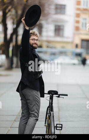 Stylish handsome hipster man riding bicycle and waving Hello. Stock Photo