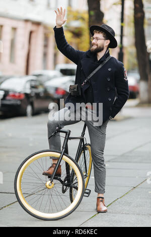 Casual handsome hipster man riding bike and waving Hello. Stock Photo