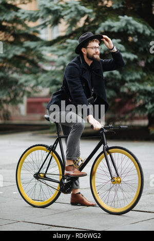 Full length photo of smiling young bearded man riding a bike on the city street Stock Photo