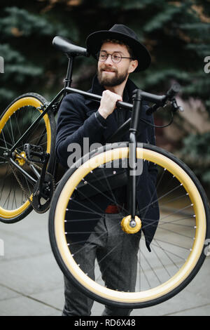 Bearded man with retro bicycle. Low angle view of confident young bearded man carrying his bicycle on shoulder and looking away while walking outdoors Stock Photo