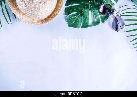 Colorful summer vacation and holiday flat-lay. Straw hat, sunglasses, palm and monstera leaves on bright blue yellow background, top view, copy space Stock Photo