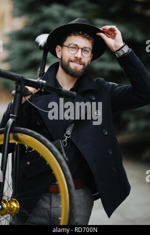 Bearded man with retro bicycle. Low angle view of confident young bearded man carrying his bicycle on shoulder and looking away while walking outdoors Stock Photo