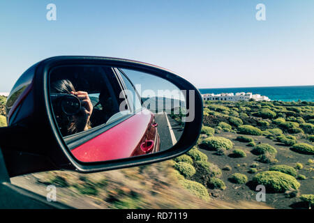 Close up of a photographer with a DSLR camera taking photo in the outside rear-view car mirror on a road trip in Lanzarote, Canary Islands, Las palmas. Stock Photo