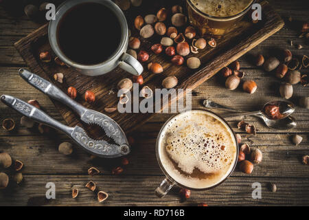 Homemade hazelnut coffee latte or cappuccino, rustic wooden background with hazelnuts, three coffee cups copy space Stock Photo