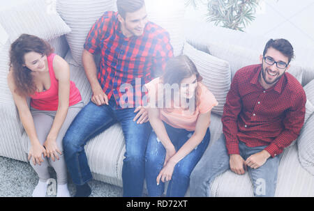 triumphant group of friends laughing while sitting on the couch in the living room Stock Photo