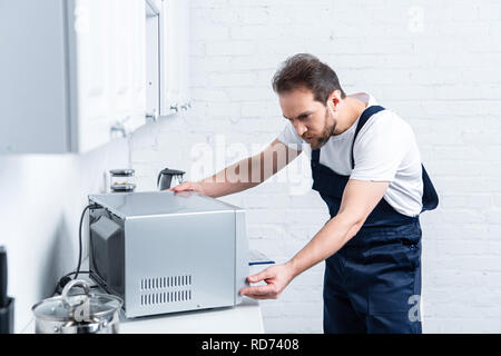 focused adult handyman repairing microwave oven in kitchen Stock Photo