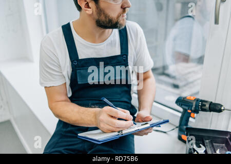 partial view of male handyman writing in clipboard and checking window Stock Photo
